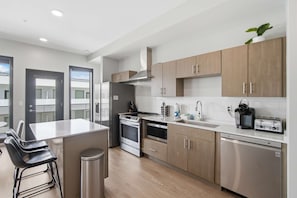 A modern kitchen with stainless steel appliances, wooden cabinets, and a bar area with stools. - Poolside Balcony, Near Downtown, In-unit Laundry (Nashville)
