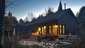 Une cabane en bois dotée d’une véranda, d’une cheminée et offrant une vue sur la forêt environnante.