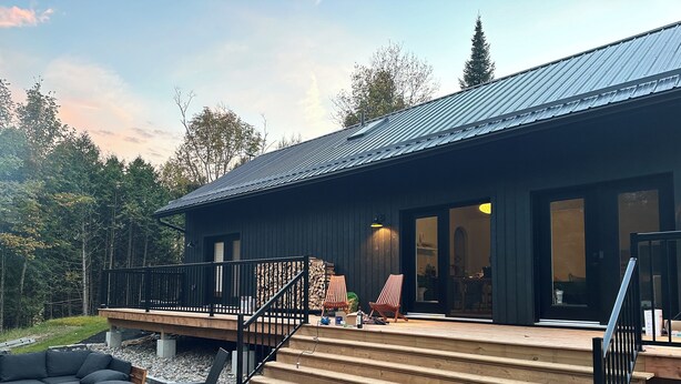 Une maison moderne dotée d’une terrasse, d’un espace salon extérieur et d’un escalier menant à l’entrée.