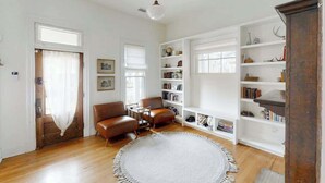 Une pièce avec un plancher en bois, un tapis rond blanc, un canapé en cuir marron, une table basse en bois et une bibliothèque.