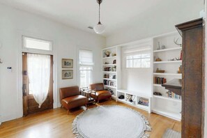 A room with a wooden floor, a round white rug, a brown leather sofa, a wooden coffee table, and a bookshelf. - 1920s Dog  Welcome Escape N East Nashville, Firepit (Nashville)