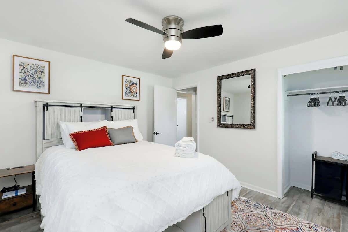 A bedroom with a bed, a ceiling fan, a mirror, and a door leading to a hallway.
