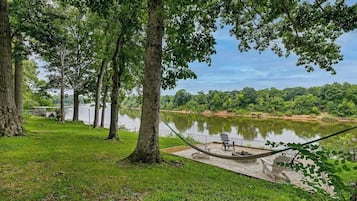 A hammock on a concrete platform by a calm lake, surrounded by trees.