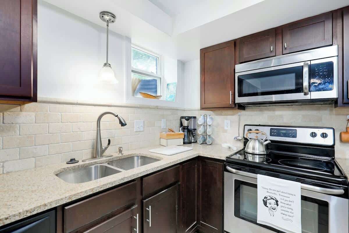 A compact kitchen with a sink, stove, microwave, and dark wooden cabinets.