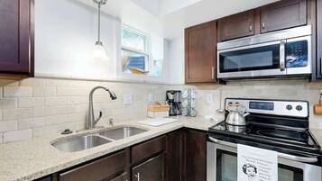 A compact kitchen with a sink, stove, microwave, and dark wooden cabinets.