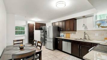 A modern kitchen with a dining area, stainless steel appliances, and a window with a view.