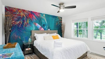 A bedroom with a bed, a ceiling fan, a window, and a large abstract painting on the wall.