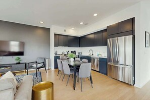 A modern kitchen with dark cabinets, a stainless steel refrigerator, and a dining area with a table and chairs. - Luxe 5th Floor Downtown Condo, Riverfront W Views (Nashville)