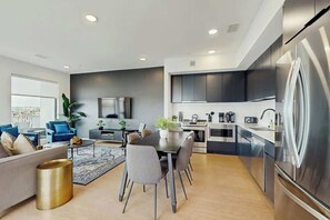 A modern kitchen with stainless steel appliances, a dining area with a table and chairs, and a living room with a sofa and a coffee table. - Luxe 5th Floor Downtown Condo, Riverfront W Views (Nashville)