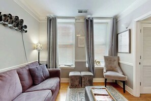 A living room with a sofa, ottoman, chair, and a wall-mounted shoe rack. - Renovated Downtown Nashville Apartment + Elevator (Nashville)
