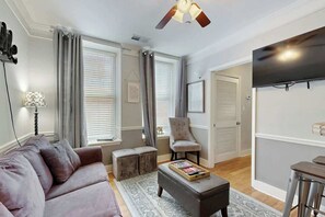 A living room with a sofa, ottoman, chair, and a flat-screen TV on the wall. - Renovated Downtown Nashville Apartment + Elevator (Nashville)