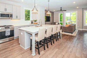 A modern kitchen with white cabinetry, a central island, and a dining area with bar stools. - Modern Nashville Escape Near Broadway・Rooftop Deck (Nashville)