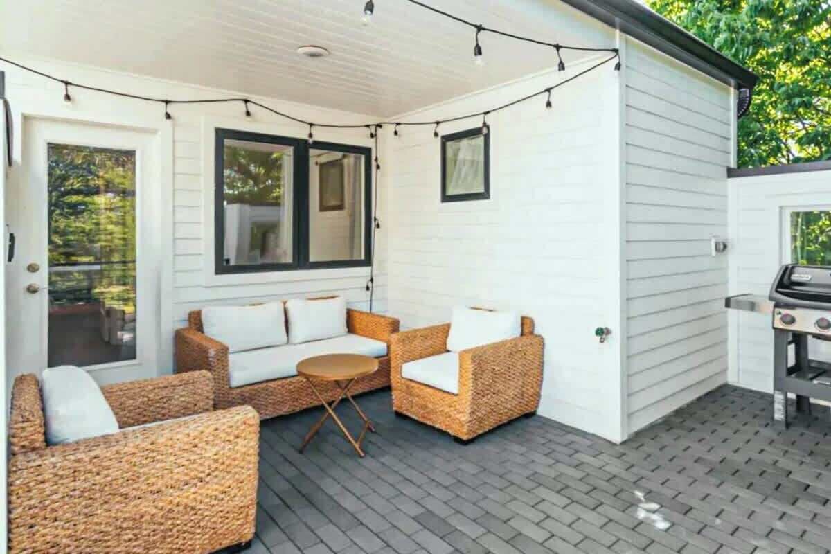 Ein überdachter Patio-Bereich mit Korbmöbeln, einem Grill und Lichterketten.