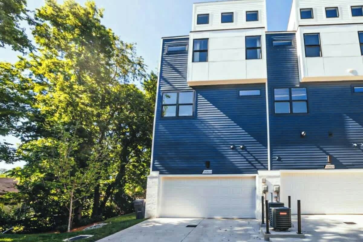 A multi-story building with a garage door, a small outdoor area with a trash bin, and a tree in the background.
