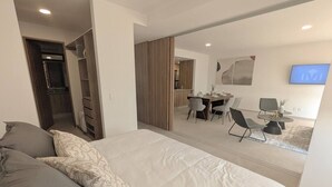 A bedroom with a large bed, a desk with chairs, a TV, and a wardrobe. - Depa de lujo en Dúo 24 | Alberca, gym y seguridad (Zapopan)