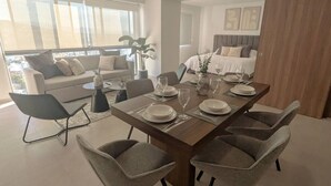 A modern dining area with a rectangular table, six grey upholstered chairs, and a sofa in the background. - Depa de lujo en Dúo 24 | Alberca, gym y seguridad (Zapopan)