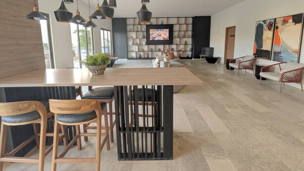 A modern kitchen with a central island, bar stools, pendant lighting, a flat-screen TV, and a decorative wall. - Depa de lujo en Dúo 24 | Alberca, gym y seguridad (Zapopan)