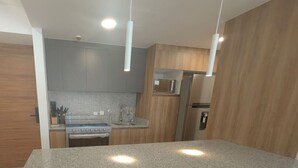 A modern kitchen with granite countertops, wooden cabinets, stainless steel appliances, and pendant lighting. - Depa de lujo en Dúo 24 | Alberca, gym y seguridad (Zapopan)