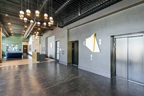 A spacious lobby with a modern design, including a reception area, elevators, and a large wall-mounted artwork. - Muse | Classy downtown condo with AC, rooftop lounge & fitness room (Nashville)