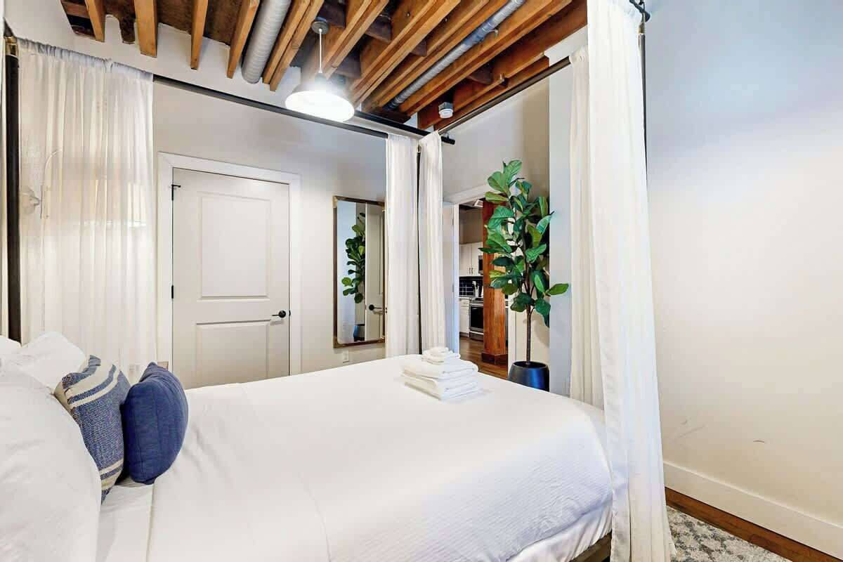 Une chambre d’hôtel avec un lit, une plante en pot, une porte et un miroir.
