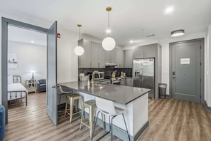A modern kitchen with a central island, bar stools, and a dining area with a table and chairs. - City Views・2BR Private Balcony・Downtown Location (Nashville)