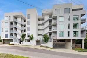 A modern multi-story residential building with balconies, a garage, and a small entrance area with a sign.