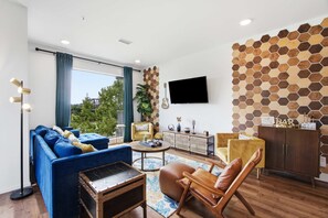 A modern living room with a sofa, armchairs, a coffee table, and a TV mounted on the wall. - Modern river-view condo with balcony & WiFi - walk to downtown & attractions (Nashville)