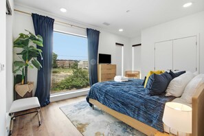 A bedroom with a bed, a TV, a plant, and a window with curtains. - Modern river-view condo with balcony & WiFi - walk to downtown & attractions (Nashville)