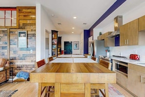 A modern kitchen with wooden cabinetry, a dining area with a long table, and a visible door leading to another room. - Dog-friendly treetop escape with luxe interior, seasonal pool, balcony, & WiFi (Nashville)