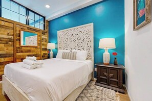 A bedroom with a large bed, a wooden accent wall, a decorative headboard, and a nightstand with lamps. - Dog-friendly treetop escape with luxe interior, seasonal pool, balcony, & WiFi (Nashville)