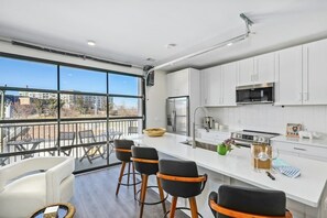 A modern kitchen with white cabinets, a stainless steel refrigerator, and a large window overlooking a balcony with outdoor seating. - City View 3rd Floor Condo Stay & Private Balcony (Nashville)