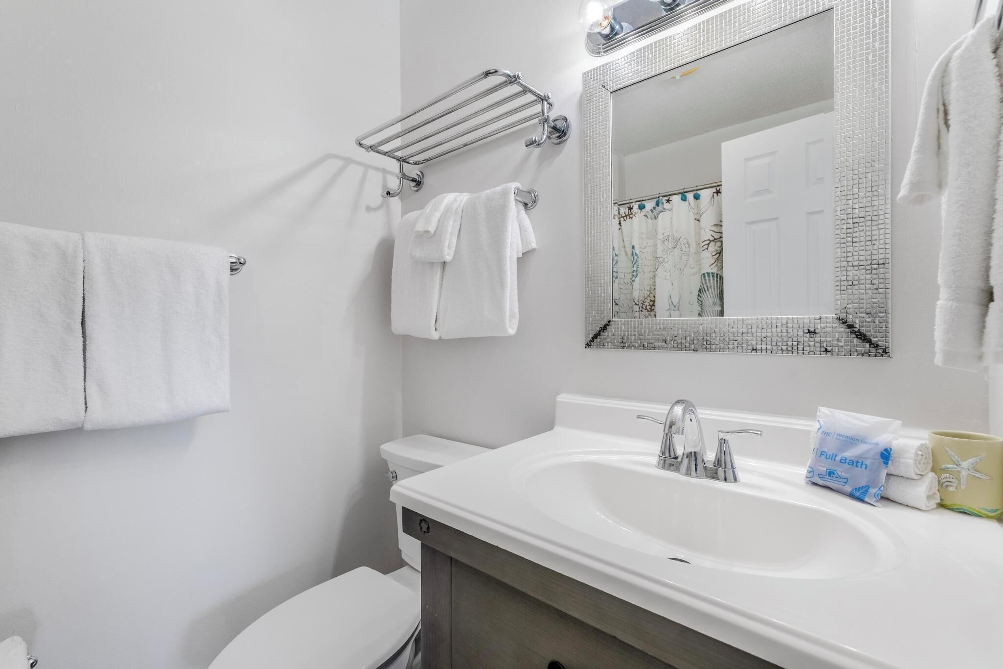 Une salle de bain avec un lavabo blanc, un miroir, un porte-serviettes et des toilettes.