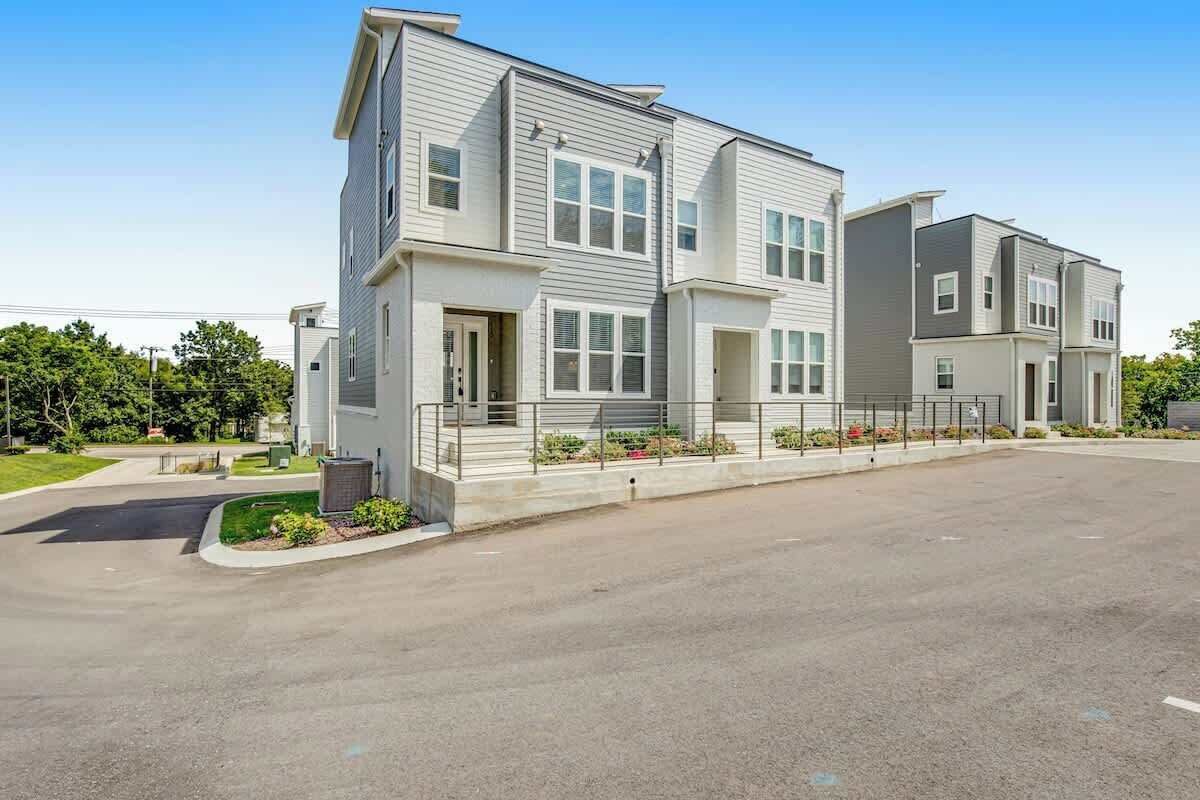 A modern multi-story residential building with a flat roof, large windows, and a paved driveway.