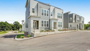 A modern multi-story residential building with a flat roof, large windows, and a paved driveway.