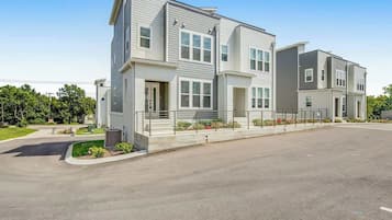 A modern multi-story residential building with a flat roof, large windows, and a paved driveway.