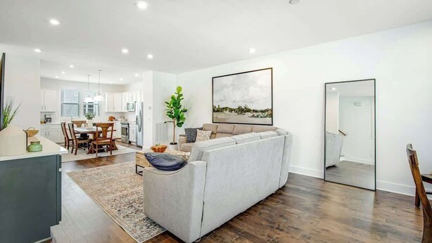 A modern living room with a sofa, dining area, and kitchen in the background.