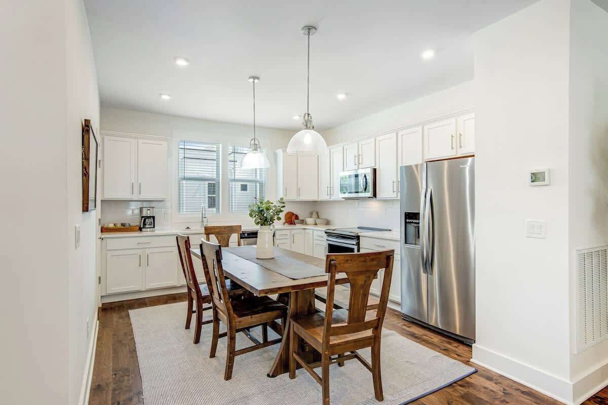 A modern kitchen with white cabinets, stainless steel appliances, and a dining area with wooden chairs and a table.