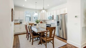 A modern kitchen with white cabinets, stainless steel appliances, and a dining area with wooden chairs and a table.