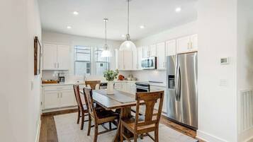 A modern kitchen with white cabinets, stainless steel appliances, and a dining area with wooden chairs and a table.