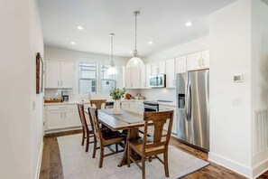 Una cocina moderna con armarios blancos, electrodomésticos de acero inoxidable y un comedor con sillas y una mesa de madera.