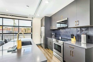 Een moderne keuken met een centraal eiland, roestvrijstalen apparatuur en een uitzicht op gebouwen door grote ramen.
