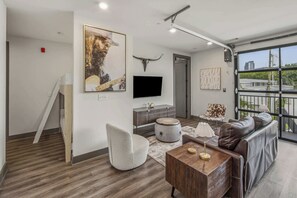 A modern living room with a sofa, ottoman, and a flat-screen TV mounted on the wall. - Sleek & Stylish condo with Shared Fitness Room (Nashville)