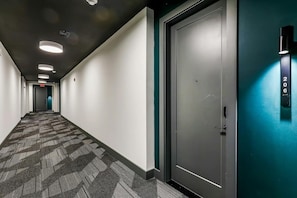 A hallway with a patterned carpet, a door with a number, and recessed ceiling lights. - Muse | Sleek & stylish condo with central AC, full kitchen & fitness room (Nashville)