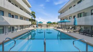 A swimming pool with a 6-inch depth marker, surrounded by lounge chairs and umbrellas, with a clear sky above.