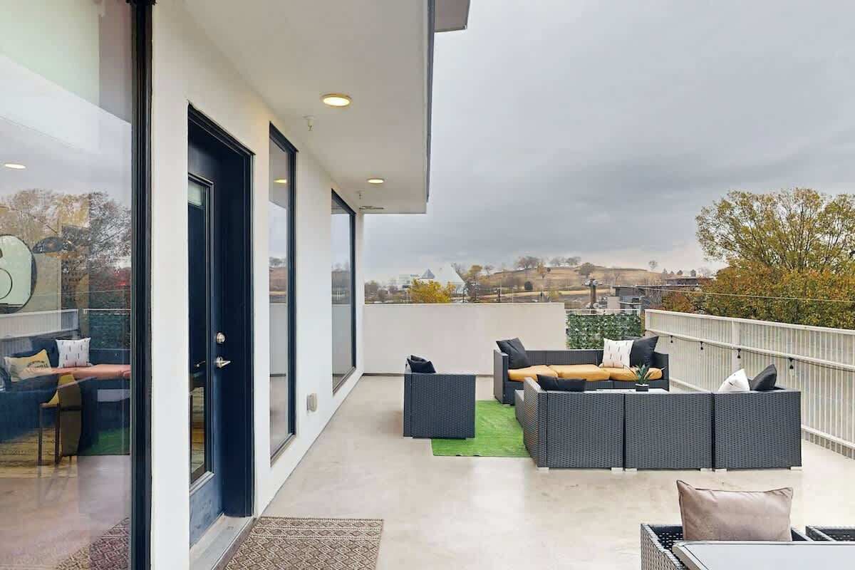 A modern balcony with outdoor seating, a glass door, and a view of the cityscape.