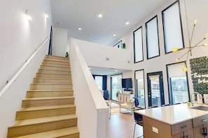 Ein modernes Interieur mit Treppe, Küchenbereich und Wohnraum mit großen Fenstern.