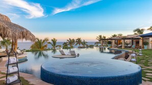 Ein Hotelpool mit Liegestühlen, einem Reedschirm und Blick auf den Ozean.