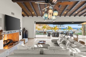 Amplia sala de estar con chimenea, un televisor de pantalla plana grande y vistas a una piscina y montañas.