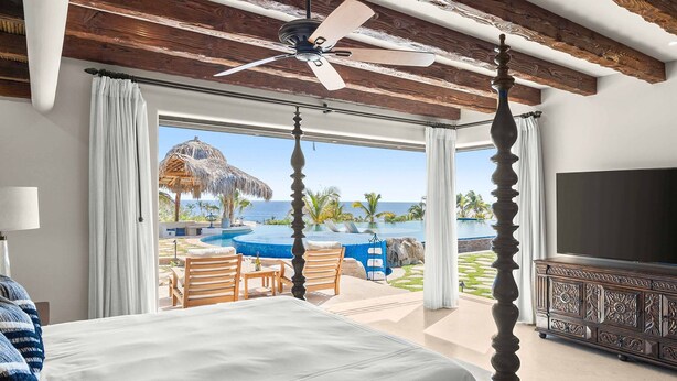 Ein Schlafzimmer mit Bett, Deckenventilator, Fernseher und Blick auf Pool und Meer.