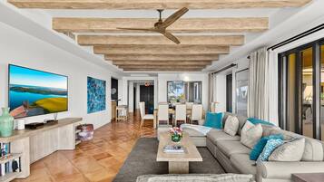 Una sala de estar moderna con un televisor grande, vigas de madera en el techo, un sofá y un comedor.